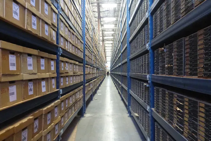 cardboard file boxes stacked on blue shelves in warehouse