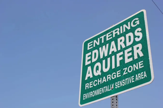 green sign with text that reads Entering Edwards Aquifer Recharge against blue sky Zone