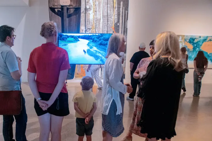people looking at video on screen in gallery during opening reception