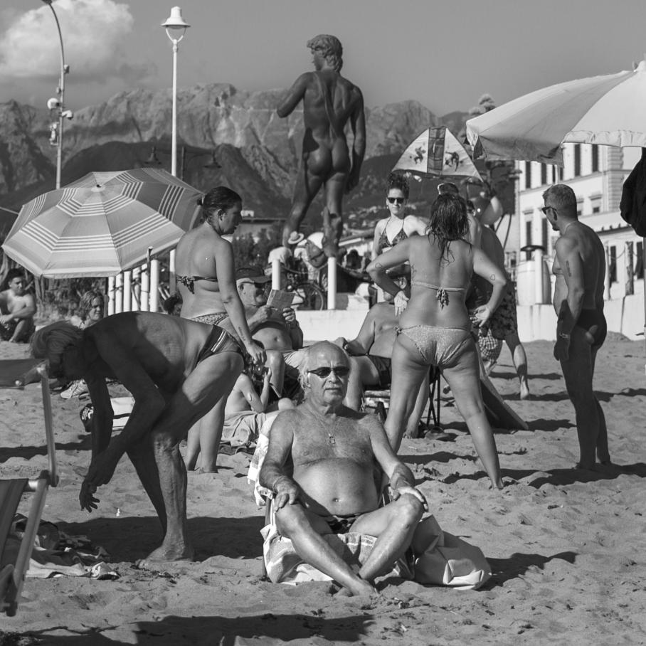 people on beach with Italian statue in background