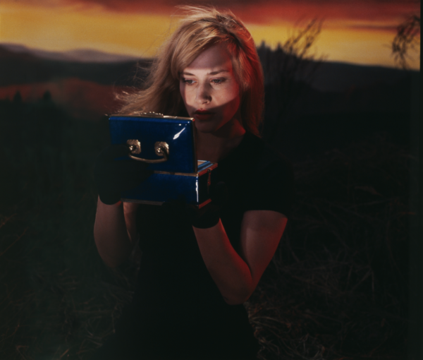 Blonde woman looking into old fashioned camera in front of a sunset
