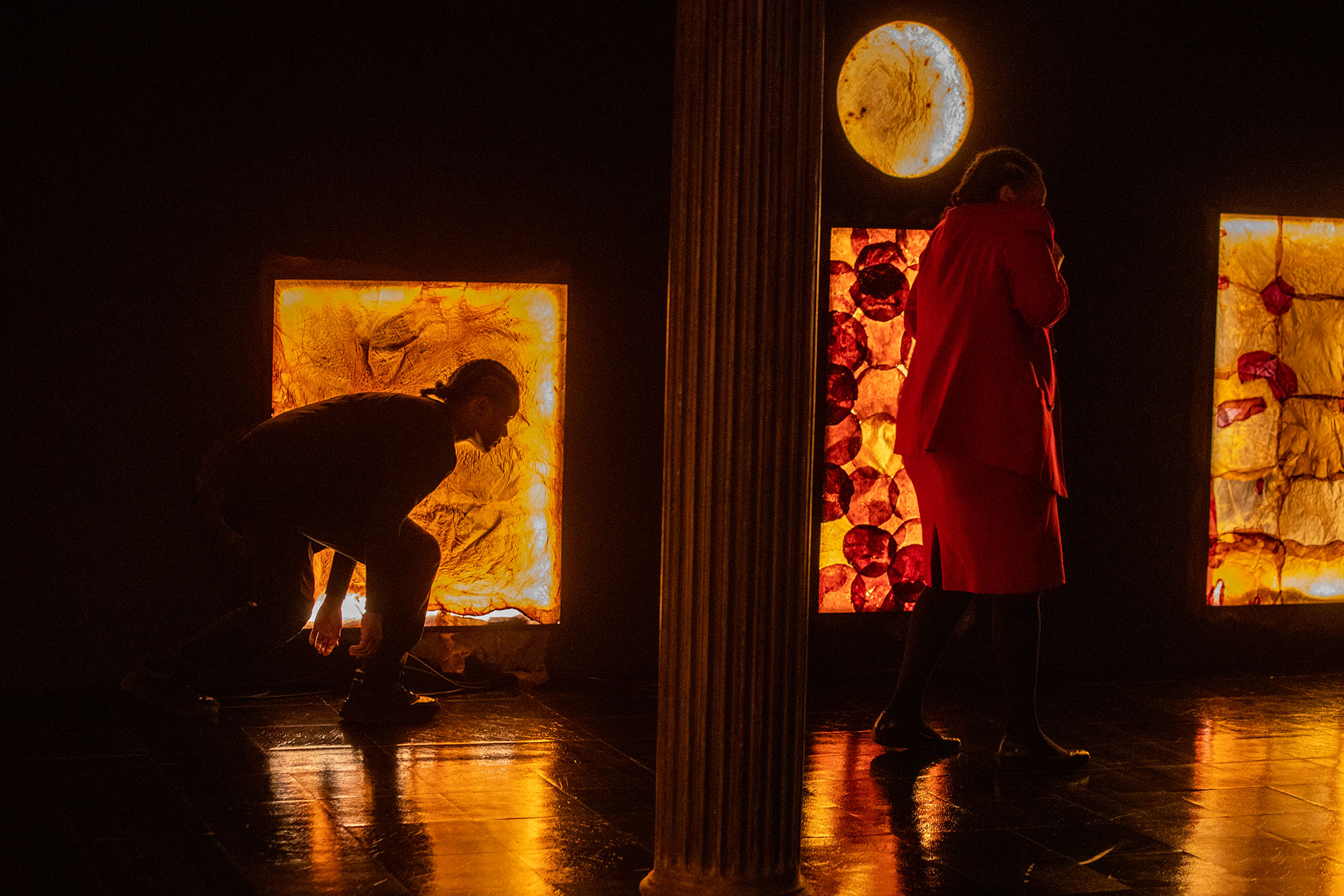 two figures in darkened space illuminated by light shining through windows