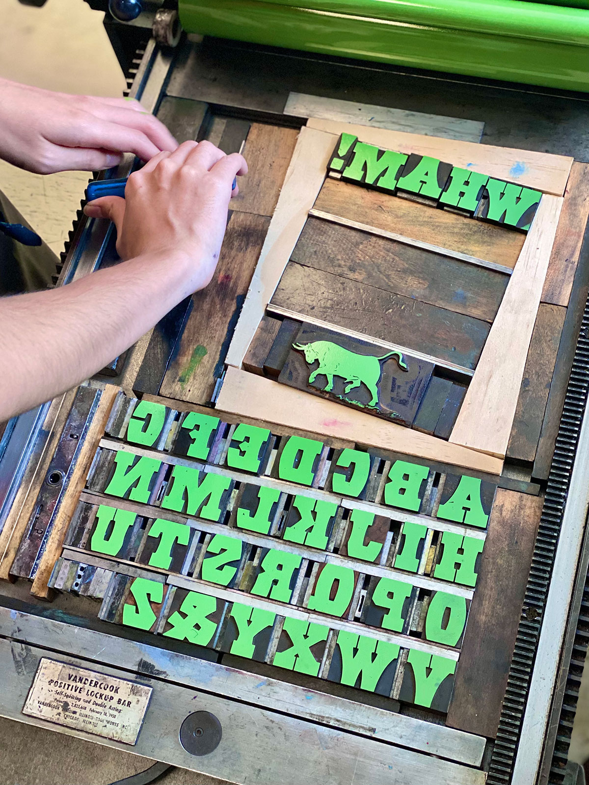 person locking up wood type on the bed of a printing press