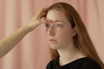 person's arm shown pushing their thumb into another person's forehead