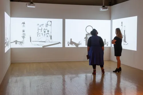 two people in gallery looking at video projections on walls