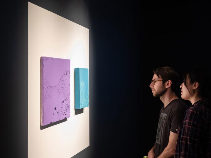 two people looking at art on the wall of a gallery