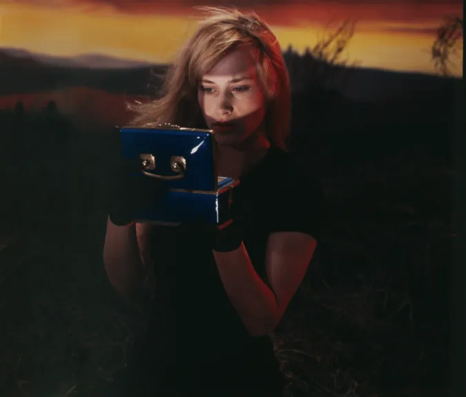 Blonde woman looking into old fashioned camera in front of a sunset